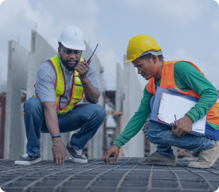Two construction workers in safety helmets inspecting reinforced steel structure for quality checks at a building site
